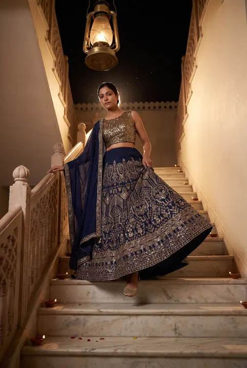 Woman in navy embroidered lehenga descending a lamp-lit marble staircase at night