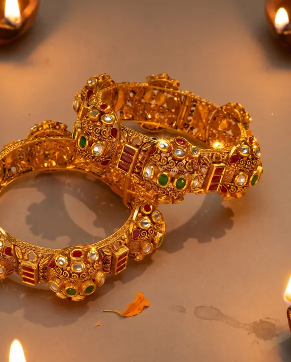 Festive pair of gold kadas among lit diyas with marigold petal on warm ground.