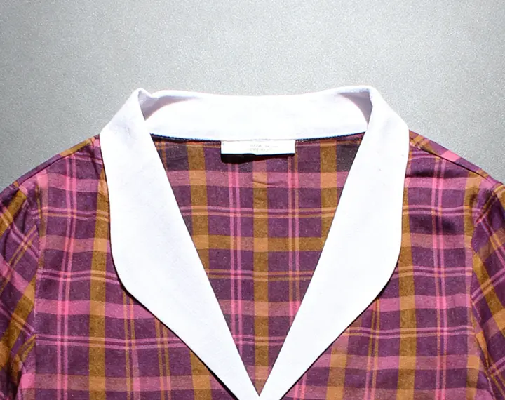 Close crop of the Sabki Madras shirt: pink, plum and mustard check with a wide white split collar, on a grey backdrop.