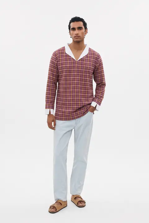 Man in the Sabki Madras shirt with pale jeans and tan sandals, plain studio backdrop, full length.