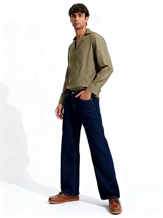 Man in the Sabki Olive shirt turned three-quarter, hand in dark jeans pocket, white studio backdrop.